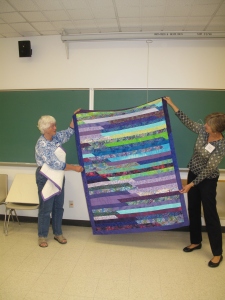 Janney, left, and Cindy, right hold up Janney's jelly roll quilt.  Yahoo!!!!